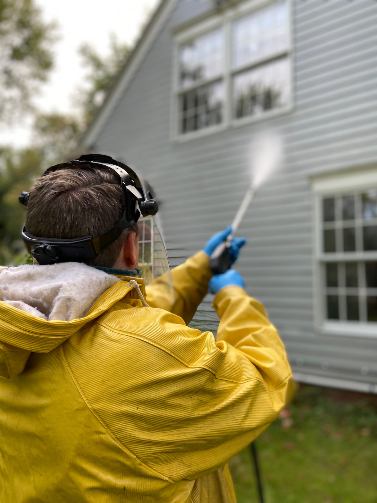 Worker applying a low-pressure rinse to house siding